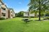 Beautiful apartment complex with charming brick facades, lush green lawns, and a peaceful outdoor seating area under a large tree.