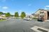 Charming apartment exterior with red brick accents, ample parking, and lush green trees under a bright blue sky.