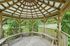 Charming wooden gazebo with a spacious seating area surrounded by lush greenery, perfect for relaxing outdoor gatherings.
