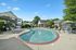 Inviting outdoor pool area surrounded by lush greenery, elegant lounge chairs, and charming residential buildings under a clear blue sky.