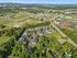 Aerial view of a vibrant residential area nestled amidst lush green landscapes, showcasing modern apartment complexes with ample parking and scenic surroundings.