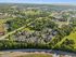 Aerial view of a charming suburban apartment complex surrounded by lush greenery, showcasing inviting residential buildings, well-maintained roads, and nearby amenities, set against a backdrop of rolling hills.