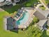 Breathtaking aerial view of a luxurious apartment complex featuring a uniquely shaped pool, surrounded by lush green landscape and charming outdoor seating.