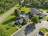 Aerial view of a picturesque apartment complex with a refreshing pool, lush green surroundings, and ample parking, offering a serene living experience.