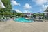 Inviting outdoor pool area with comfortable lounge chairs, shaded seating, and lush greenery under a clear blue sky.