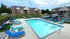 Inviting outdoor pool area with vibrant blue loungers, umbrellas, and scenic apartment buildings in the background.