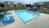 Inviting apartment community pool area with modern lounge chairs, surrounded by well-maintained grounds and brick buildings.