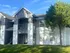 Charming two-story apartment building with a cozy balcony, surrounded by lush greenery and a bright blue sky.