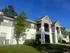 Charming two-story apartment building with modern balconies and lush green surroundings under a bright blue sky.
