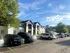Serene apartment complex with modern white exteriors nestled amidst lush greenery and a sunlit sky.
