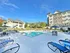 Inviting residential complex with a sparkling outdoor pool, lounge chairs, and umbrella-shaded tables, set against a backdrop of modern apartment buildings and lush greenery.