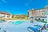 Vibrant apartment complex featuring a large pool surrounded by comfortable lounge chairs and modern buildings under a clear blue sky.