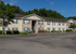 Charming apartment complex with lush landscaping and ample parking, set against a backdrop of greenery and blue skies.