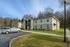Modern apartment building with well-maintained landscaping, ample parking, and scenic wooded backdrop.