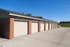 Charming row of brick garages with pristine driveways and a serene blue sky backdrop, offering ample parking and storage space.