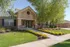 Charming apartment entrance with manicured garden, vibrant flowers, and lush green lawn under a clear blue sky.