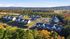 Expansive aerial view of a serene apartment community surrounded by lush greenery and vibrant fall foliage with a beautiful landscape and modern residences.