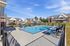 Charming apartment complex featuring a sparkling pool surrounded by modern lounge chairs and vibrant greenery.