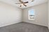 Bright bedroom with soft gray carpet, modern ceiling fan, and a window revealing scenic views.