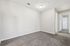 Bright empty room with plush gray carpet, freshly painted white walls, and a ceiling light fixture leading to a hallway with multiple doors, offering ample design possibilities.