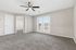 Bright and spacious living room with plush carpeting, ceiling fan, and double glass doors leading to a scenic balcony view.
