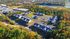 Aerial view of a charming apartment complex surrounded by lush greenery and a serene lake, showcasing multiple buildings, spacious parking areas, and a scenic neighborhood setting.