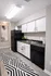 Modern kitchen featuring sleek black and white cabinetry, elegant light fixture, and a stylish geometric rug.