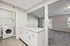 Bright apartment interior featuring a sleek laundry area with modern washer, adjacent to a spacious living room with plush carpet and abundant natural light.