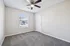 Bright empty room with plush carpeting, modern ceiling fan, and a large window filling the space with natural light.