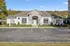 Charming clubhouse exterior in serene surroundings, featuring neatly maintained landscaping and ample parking spaces.