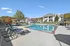 Inviting outdoor pool area with modern lounge chairs and umbrellas, surrounded by lush greenery and stylish apartment buildings under a clear blue sky.