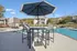 Inviting poolside oasis with stylish outdoor seating under a large umbrella, set against a backdrop of charming residential buildings and vibrant autumn foliage.