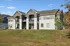 Charming two-story apartment complex with modern gray and white facade, featuring private balconies, nestled in serene green surroundings.