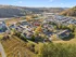 Charming aerial view of a vibrant residential community surrounded by lush greenery and scenic hills, showcasing modern multi-story apartment buildings under a clear blue sky.