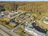 Aerial view of a beautiful apartment community nestled in lush greenery, featuring modern buildings, ample parking, and a sparkling swimming pool. Scenic wooded backdrop enhances the serene living environment.