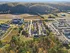 Aerial view of a vibrant residential community surrounded by lush greenery and rolling hills, showcasing modern apartment buildings and scenic natural beauty.