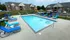 Inviting outdoor pool area with bright blue lounge chairs, surrounded by charming brick apartments and lush green landscaping.