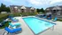 Inviting swimming pool area with modern lounge chairs, vibrant blue umbrellas, and a backdrop of contemporary brick apartment buildings, perfect for relaxation and leisure.
