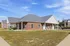 Charming brick apartment with a spacious front lawn and inviting covered porch, set under a clear blue sky.