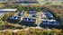 Aerial view of a picturesque apartment complex surrounded by lush greenery and vibrant fall foliage, complete with spacious parking and nearby serene lakes.