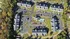 Aerial view of a beautifully arranged apartment complex with multiple buildings, a central swimming pool, ample parking, and lush green surroundings.