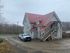Charming multi-story house with a striking red metal roof, featuring a rustic outdoor staircase and ample parking space, set against a backdrop of serene woodland.
