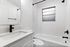 Elegant bathroom with a modern monochrome design, featuring a sleek white vanity, matte black fixtures, and a tastefully tiled bathtub area.