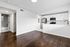 Modern apartment with sleek hardwood floors and a bright open-concept kitchen featuring white cabinets and stainless steel appliances.
