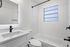 Bright, modern bathroom with sleek white fixtures, elegant black accents, and a large frosted window for natural light.
