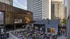 Vibrant city plaza with outdoor movie screening under string lights, surrounded by towering buildings and lively crowd.