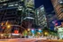 Vibrant nighttime cityscape showcasing modern skyscrapers with glowing windows, busy streets, and dynamic light trails in the heart of an urban setting.