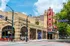Charming street view of a historic brick theater with vibrant signage, nestled on a bustling city corner with lush trees and flags.