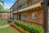 Charming brick apartment building with elegant wrought-iron details, lush landscaping, and expansive green lawn, offering serene and stylish living.