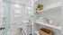 Bright, modern bathroom featuring a sleek walk-in shower, elegant vanity, and stylish open shelving with cozy towels and decorative jars.
